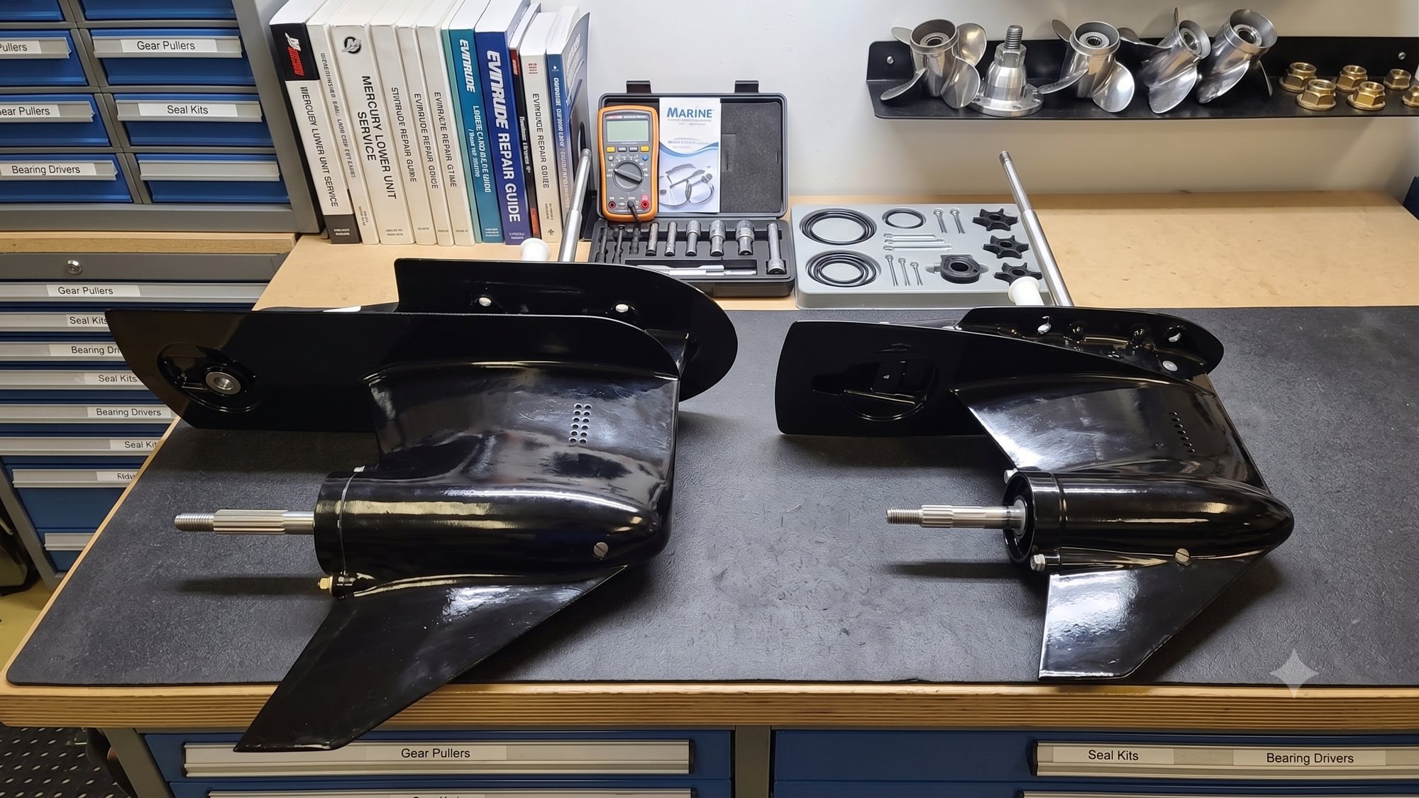 Mercury Command Thrust gearcase next to a standard gearcase on the Harris Boat Works service bench, showing the size difference in the torpedo housing and skeg